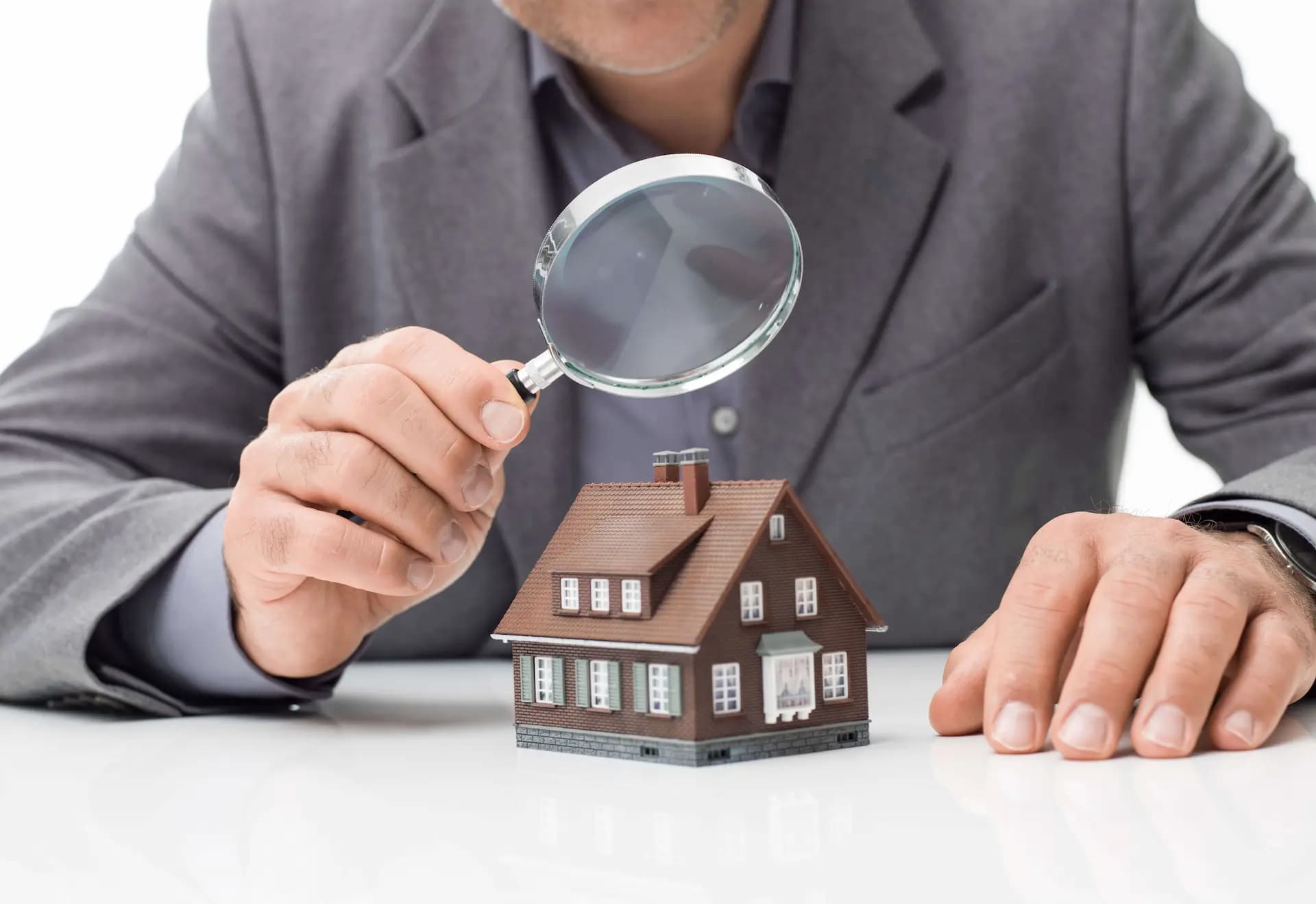 diagnostiqueur immobilier — un expert passant une maison miniature à la loupe